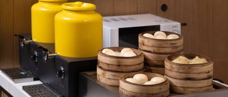 A kitchen area with a coffee machine, two yellow gas cylinders, and several bamboo steamers with dumplings.