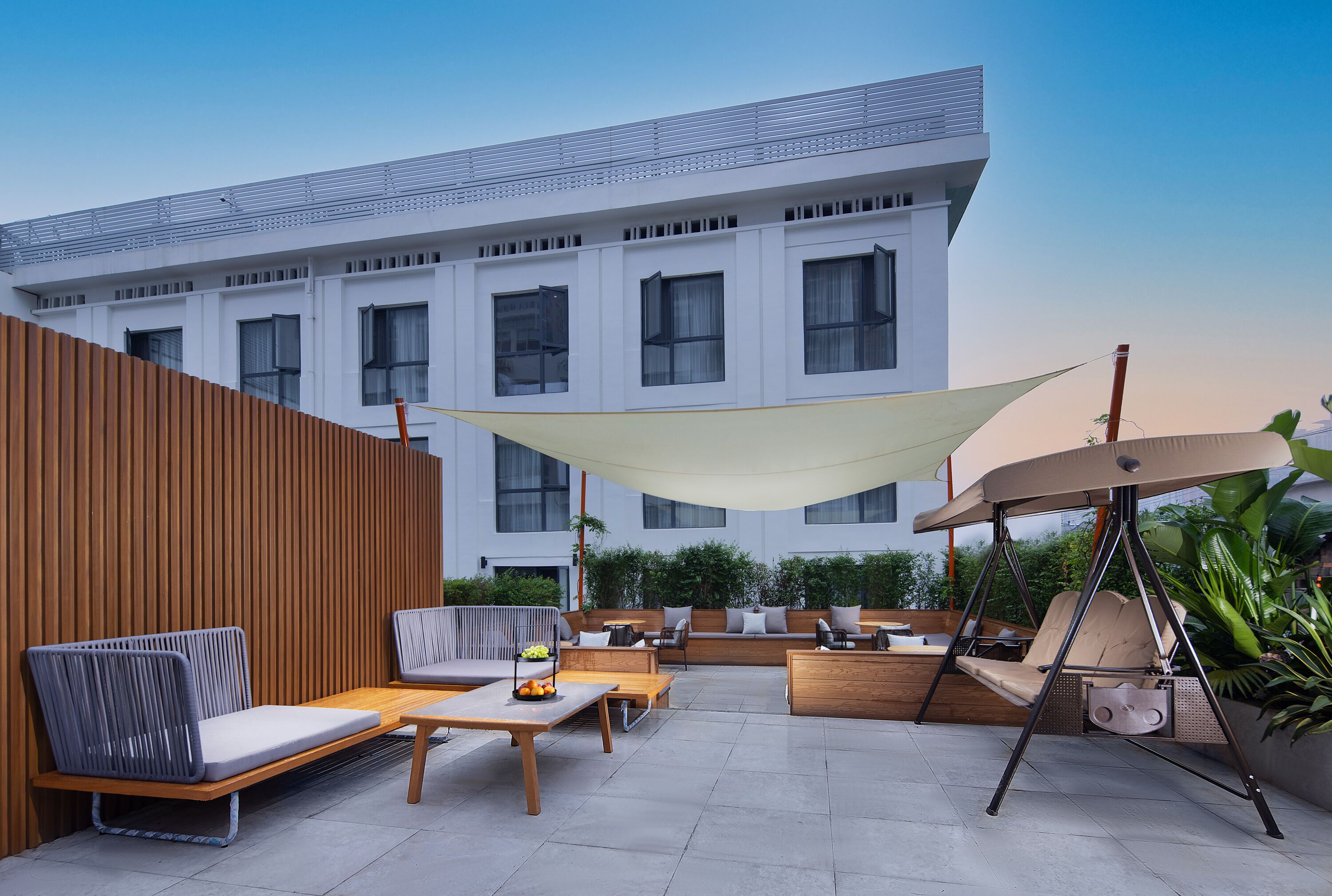 A modern outdoor seating area with a swing chair, cushioned benches, and a table with fruit.