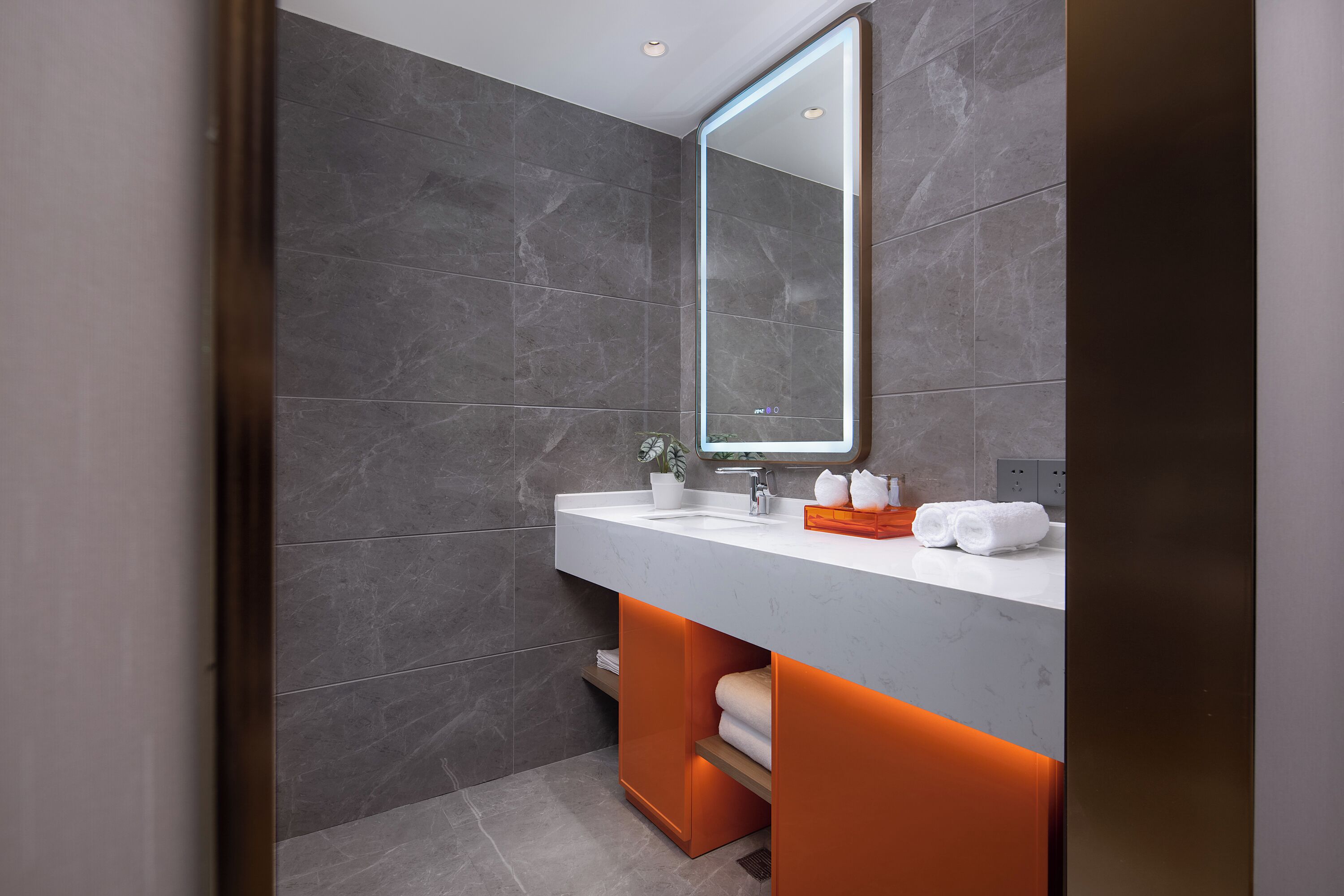 A modern bathroom with a large mirror, white countertop, and orange under-sink storage.