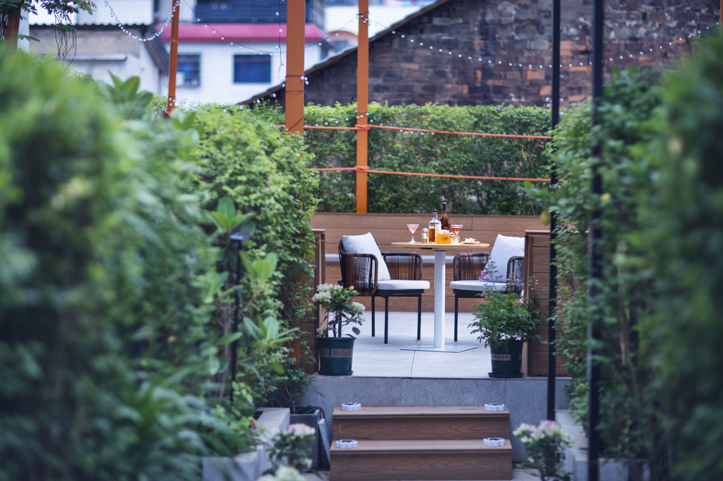 An outdoor patio area with a table and chairs, surrounded by greenery and a brick wall.