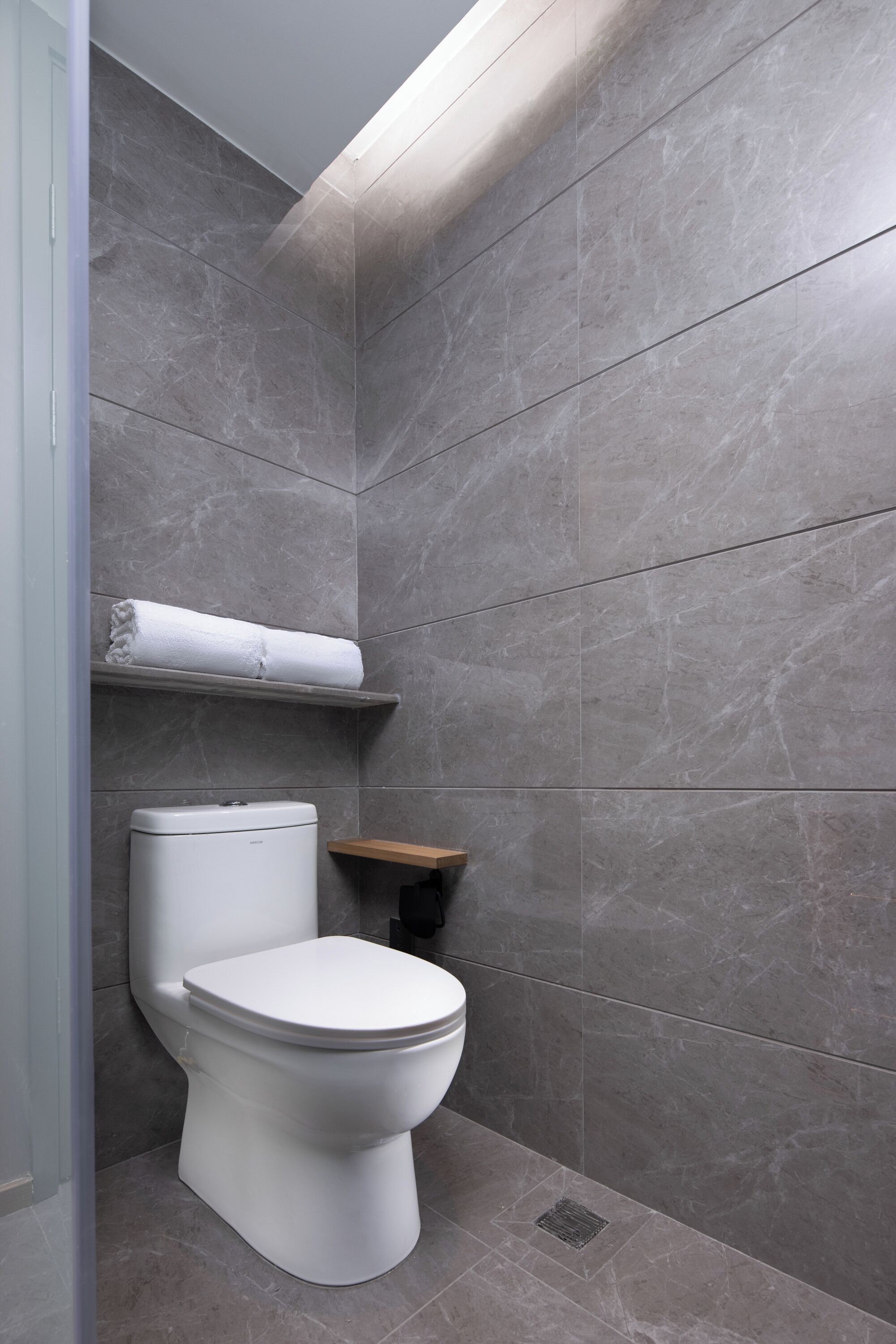 A modern bathroom with a toilet, a towel shelf, and a wooden shelf.