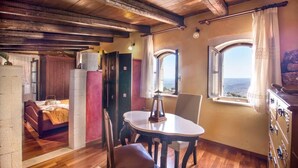 A rustic room with wooden floors, a bed, a table with chairs, and two windows with curtains.