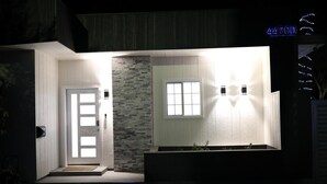 Une entrée moderne, avec un mur en pierre, une porte blanche et une fenêtre agrémentée d’un luminaire.