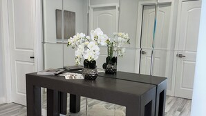 Une pièce moderne avec une table en bois foncé, des murs blancs et un grand miroir qui reflète l’espace.