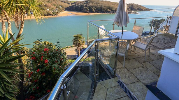 A balcony with a glass railing overlooking a beach and ocean. - 2 Channel View (Salcombe)