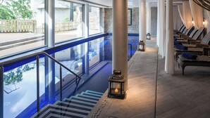 A serene indoor pool area with a clear view of the outside, a set of stairs leading down to the pool, and a row of lounge chairs with cushions. - 2 Channel View (Salcombe)