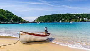 A boat tied to a sandy beach with clear turquoise water and green hills in the background. - 2 Channel View (Salcombe)