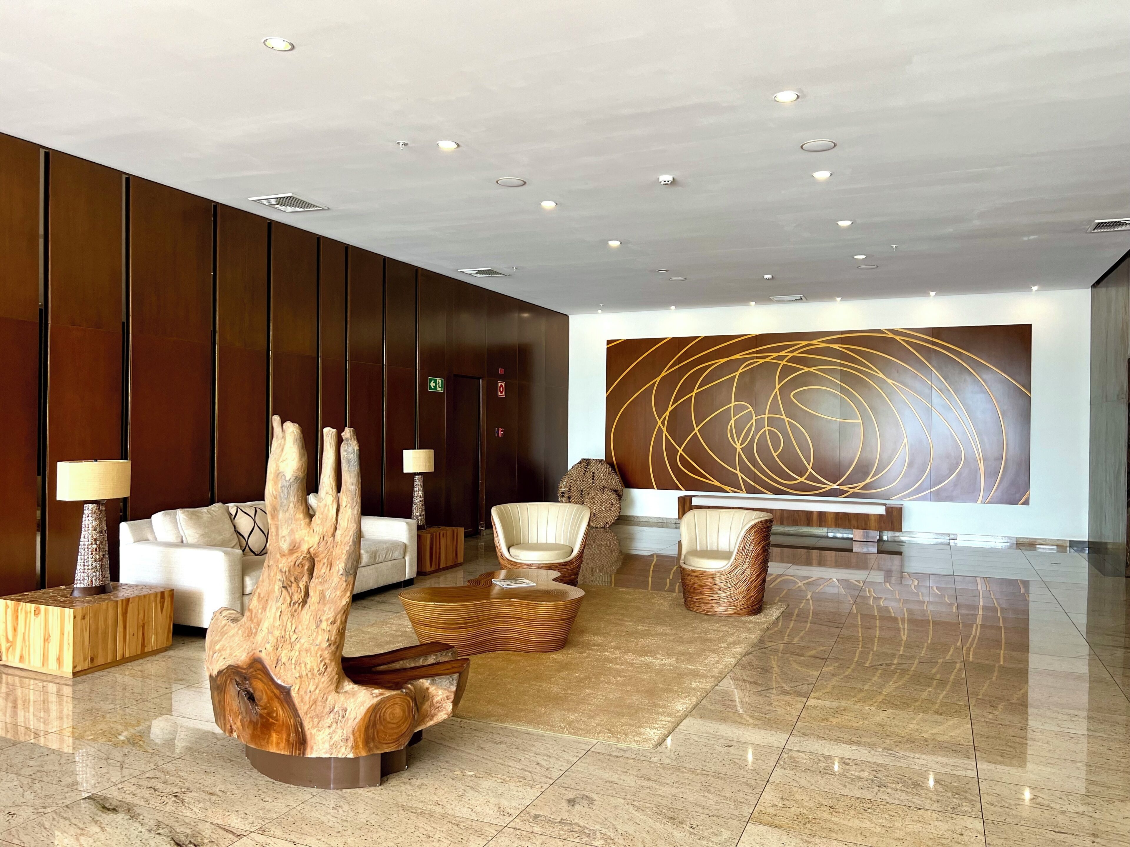 A modern lobby with a wooden reception desk, seating area, and a large abstract wall art piece.
