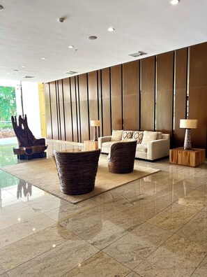 A modern lobby with a sofa, two wicker side tables, a decorative sculpture, and a wooden partition wall.