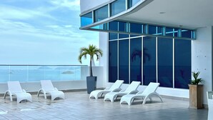 A modern rooftop terrace with white lounge chairs, large windows, and a view of the sea. - APARTMENT  BETWEEN OCEAN AND RAIN FOREST - Beachside apartment with outdoor pool (Panama City)