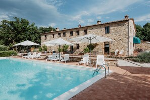 A stone building with a swimming pool, white lounge chairs, and umbrellas. - Borghetto Poggio Bianco - Antico casale (Radicondoli)