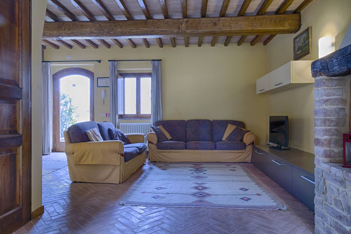 A living room with two sofas, a herringbone-patterned rug, wooden flooring, a stone fireplace, and a wooden ceiling.