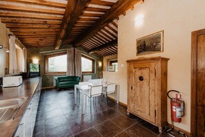 A rustic kitchen with a wooden ceiling, a green sofa, a dining table with chairs, a white cabinet, and a fire extinguisher. - Borghetto Poggio Bianco - Antico casale (Radicondoli)