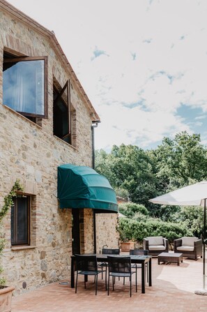 A stone building with a patio area featuring outdoor furniture and umbrellas. - Borghetto Poggio Bianco - Antico casale (Radicondoli)