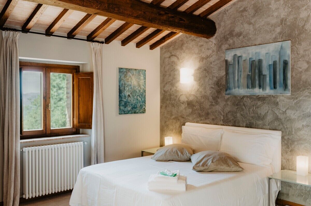 Ein Schlafzimmer mit Bett, Fenster, Heizkörper, einem Gemälde und einer Wandleuchte.