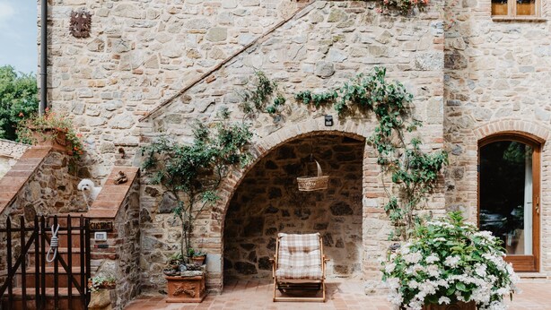 A stone building with a rustic stone wall, a wooden bench, a wicker basket, and potted plants.