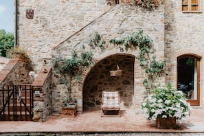 Un edificio de piedra con una pared de piedra rústica, un banco de madera, una cesta de mimbre y plantas en macetas.