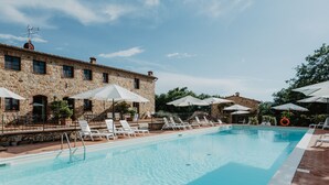 A pool area with lounge chairs and umbrellas, a stone building with windows, and a clear sky.