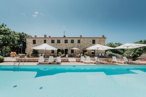A stone building with a swimming pool, outdoor seating, and umbrellas. - Borghetto Poggio Bianco - Antico casale (Radicondoli)