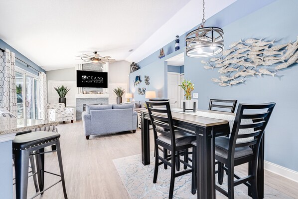 A modern kitchen with a dining area, featuring a large island, bar stools, and a blue accent wall with nautical decor.