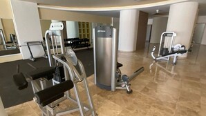 Un gimnasio con equipo de ejercicio, incluyendo una prensa de banca, una estructura para sentadillas y una máquina de poleas.