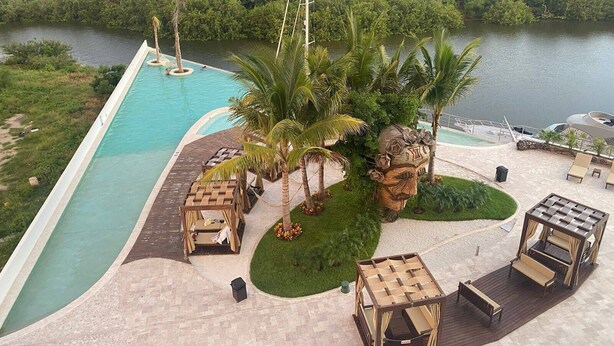 Piscina con terraza de madera, sillas de descanso y vistas al río y al paisaje urbano.