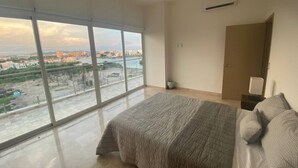 Un dormitorio con un ventanal grande, una cama, una mesita de noche y un equipo de aire acondicionado.