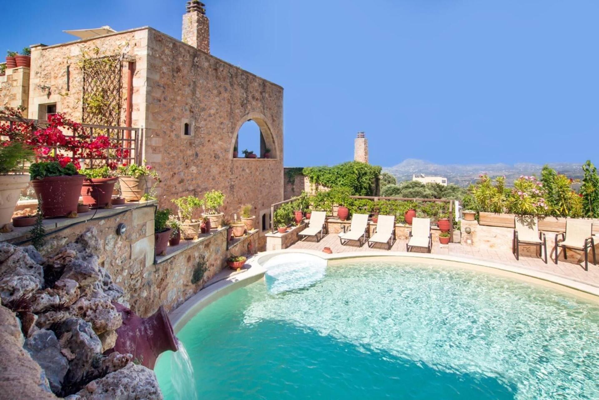 A stone building with a pool, lounge chairs, and potted plants.
