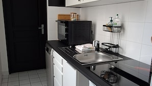 A modern kitchen with white cabinets, a black countertop, a microwave, and a sink. - Apartment in the Rotonde district (Vichy)