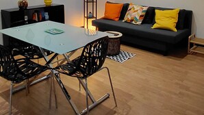 A modern living room with a dining table, black chairs, a sofa with colorful cushions, a floor lamp, and a large mirror on the wall. - Apartment in the Rotonde district (Vichy)