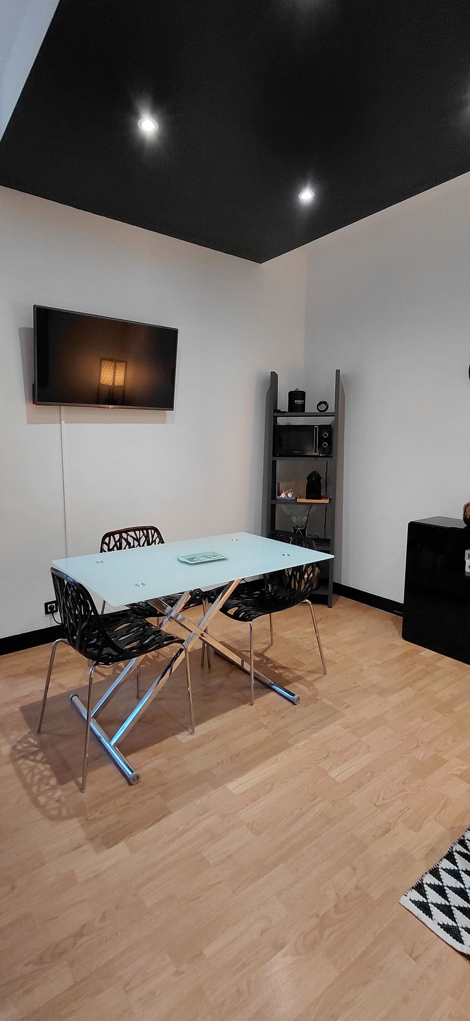 Un espace repas moderne comprenant une table, des chaises, un téléviseur fixé au mur et une étagère intégrée pour un four à micro-ondes.