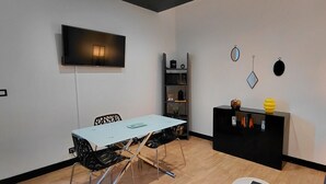 A modern living space with a flat-screen TV, a dining table with chairs, a black console table with decorative items, and a bookshelf. - Apartment in the Rotonde district (Vichy)