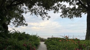 A wooden pathway leading to a beach, surrounded by lush greenery and flowering plants. - Cottage on the Bay (Saint Leonard)