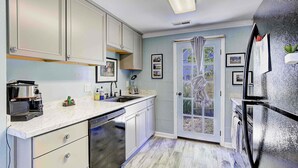A kitchen with white cabinets, a dishwasher, a refrigerator, and a window with curtains. - Cottage on the Bay (Saint Leonard)