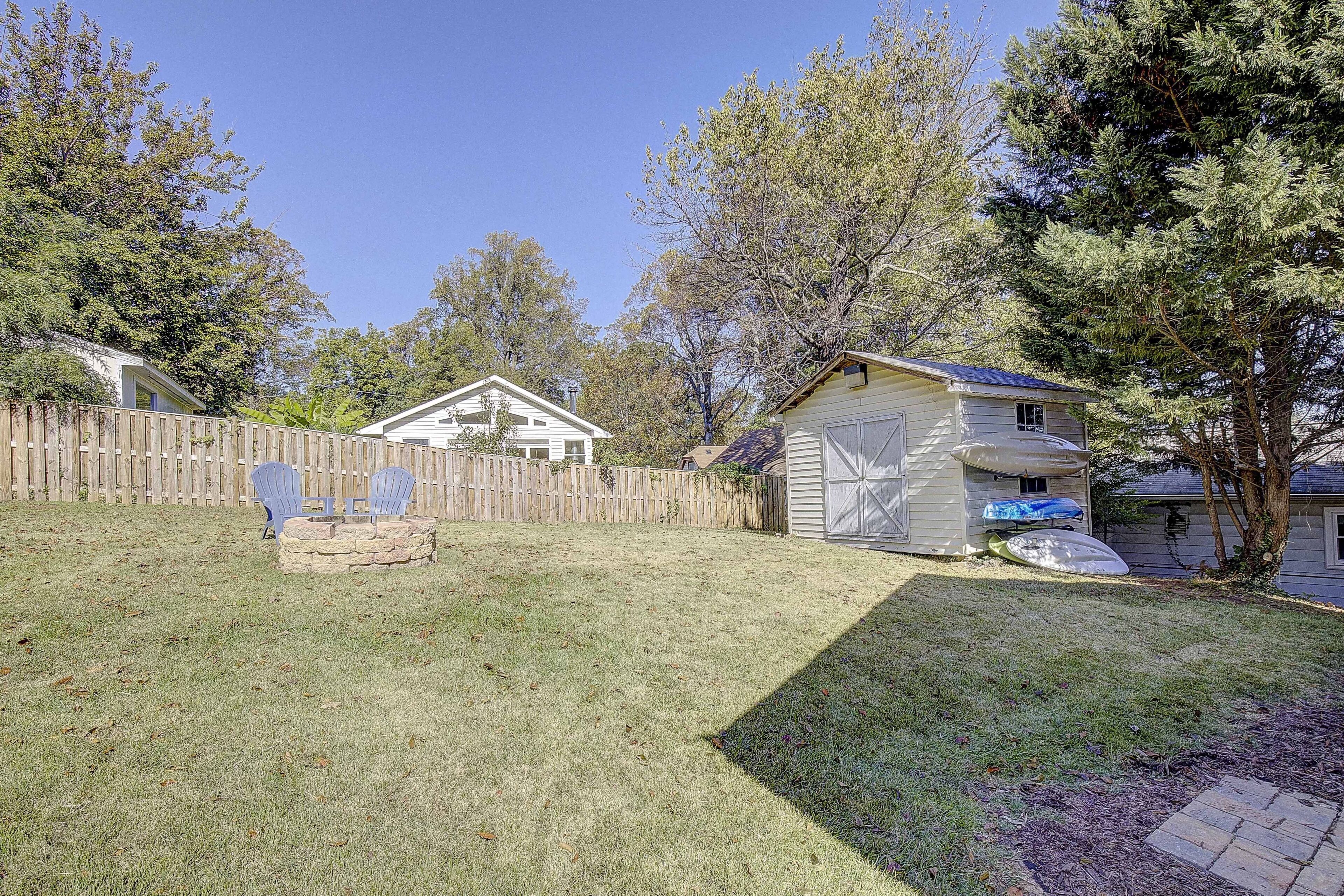 A backyard with a wooden fence, a stone fire pit, and a house with a garage.