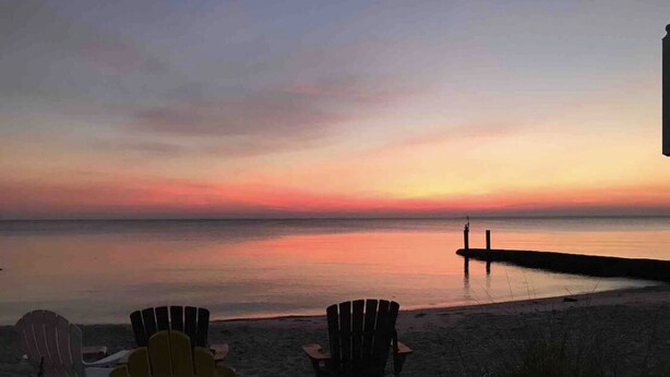 A beach with chairs and a pier extending into the water during sunset. - Cottage on the Bay (Saint Leonard)