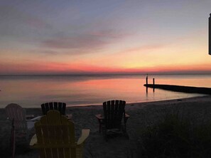 A beach with chairs and a pier extending into the water during sunset. - Cottage on the Bay (Saint Leonard)