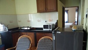 Una cocina compacta con armarios de madera, un microondas, un refrigerador y dos sillas con diseño estampado.