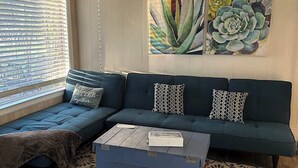 Un salón con un sofá modular, una mesa de centro y un ventanal con persianas.