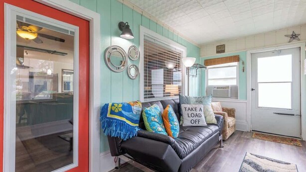 Una sala de estar acogedora con un sofá de cuero negro, almohadones de colores y un letrero que dice 'TAKE A LOAD OFF'.