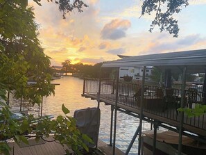 Ein Uferdeck mit Sonnenuntergangsblick, eine Bootsanlegestelle und ein Gebäude gegenüber dem Wasser.