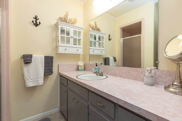 A bathroom with a sink, mirror, and cabinets. There is a towel rack with towels, a tissue box, and a soap dispenser.