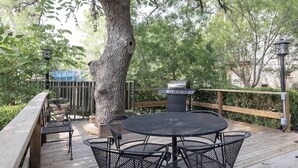 Un patio al aire libre con una mesa redonda y sillas, una parrilla y un piso de madera.