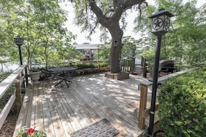 A wooden deck with outdoor furniture, a large tree, and a grill area.