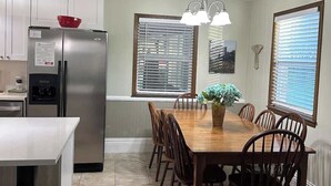 Una cocina moderna con un refrigerador de acero inoxidable, una mesa de comedor de madera y sillas, y una lámpara colgante sobre la mesa.