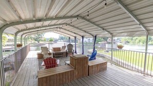 Una terraza techada con mobiliario de madera, incluyendo sillas y una mesa, con vista a un cuerpo de agua.