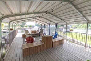 A covered deck with wooden furniture, including chairs and a table, overlooking a body of water.