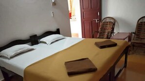 A single bed with a wooden frame, a beige bedspread, and two pillows. There is a wooden nightstand with a brown tray on it.