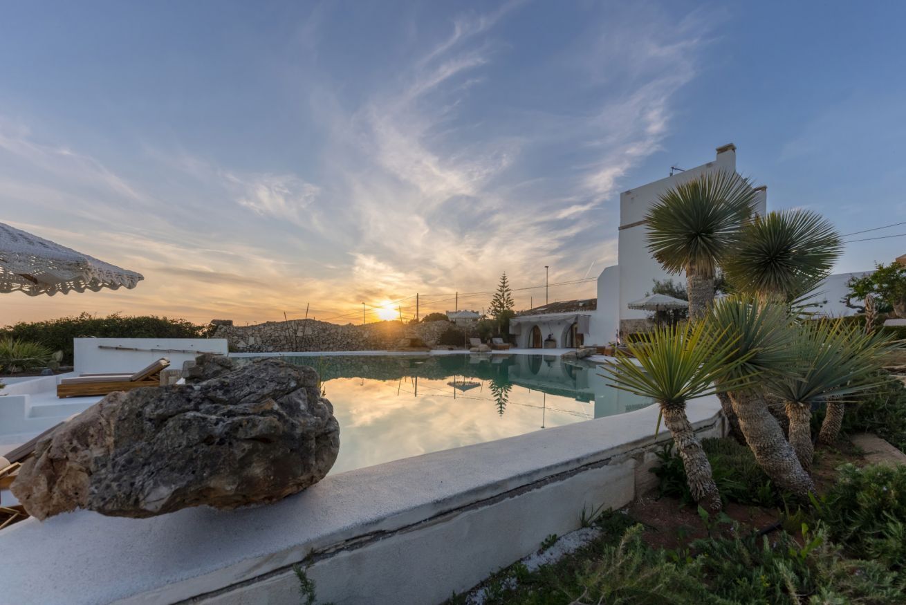 A pool area with a large rock, white buildings, and palm trees.