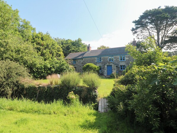A stone house with a blue door, surrounded by lush greenery and a small stream. - Sunnyvale Cottage (Penzance)